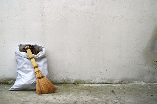 small broom and white debris bag leaning against a white wall